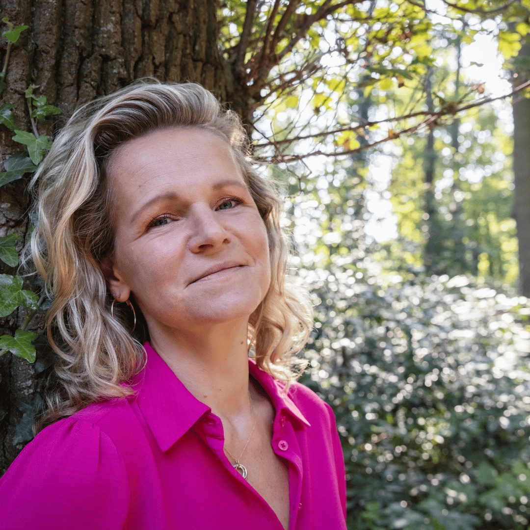 Esther in een roze blouse tegen een boom in het bos